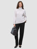 En kvinne i en lys turtleneck og Women GO2 Pants Straight Black, som holder en håndveske i minimalistisk skandinavisk stil.