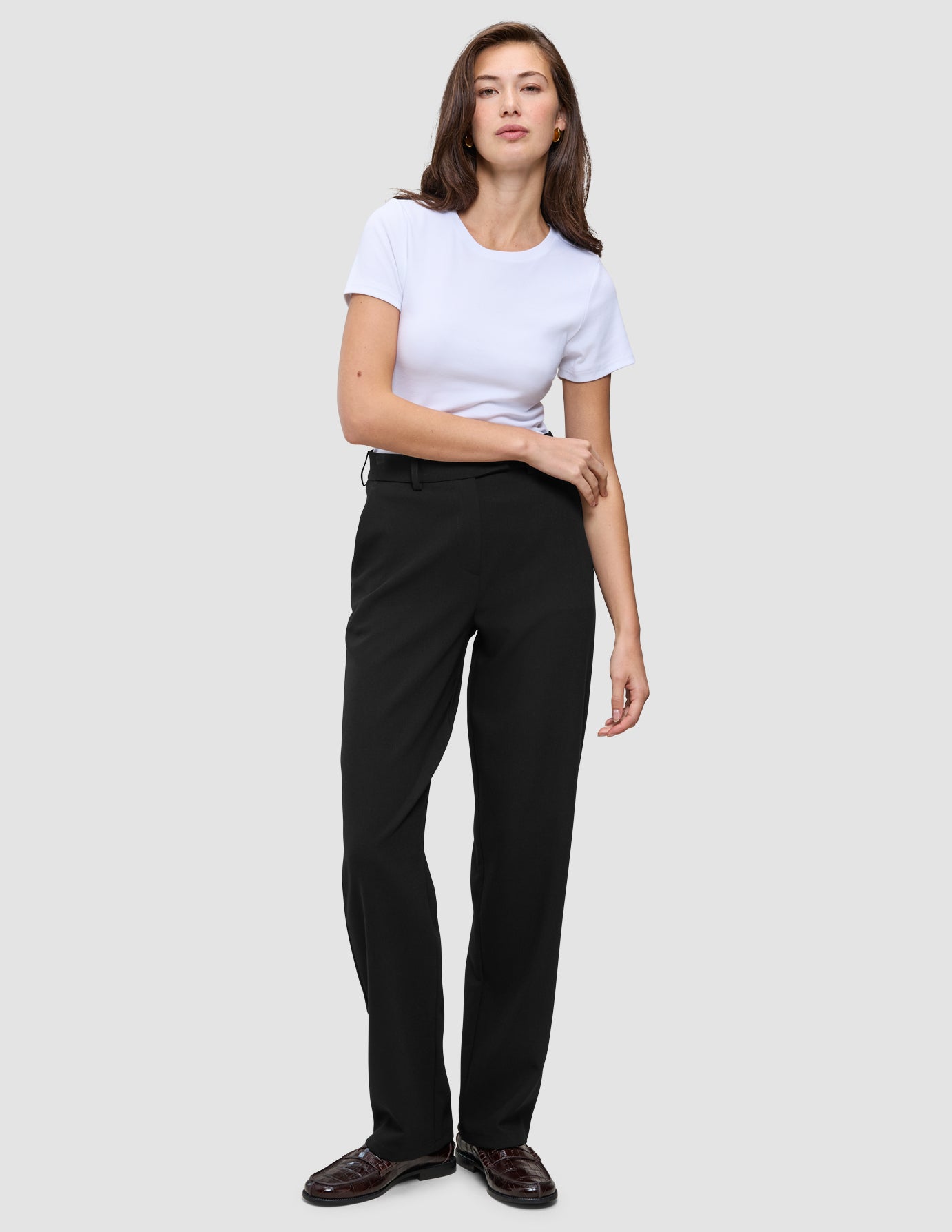 Kvinne kledd i en hvit T-skjorte, Women GO2-bukser i rett snitt i svart og mørke loafers i minimalistisk skandinavisk stil.