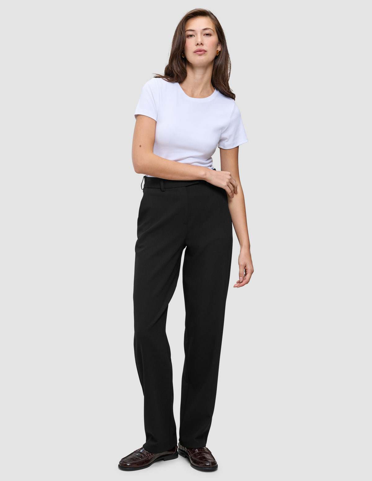 Kvinne kledd i en hvit T-skjorte, Women GO2-bukser i rett snitt i svart og mørke loafers i minimalistisk skandinavisk stil.