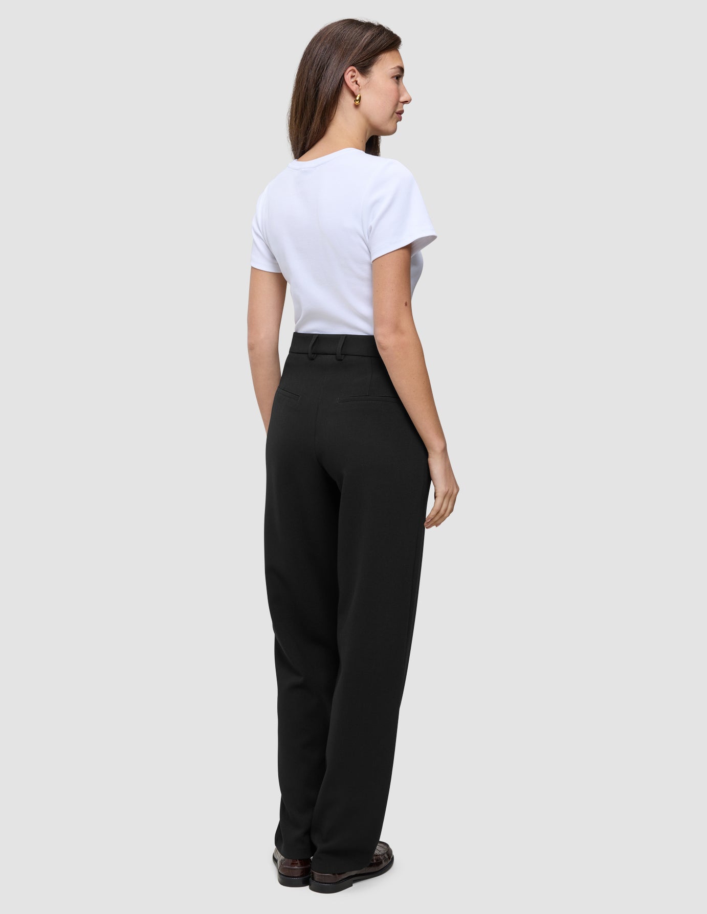 En kvinne sett bakfra, kledd i en hvit T-skjorte og svarte Women GO2 Pants Straight med rett snitt.
