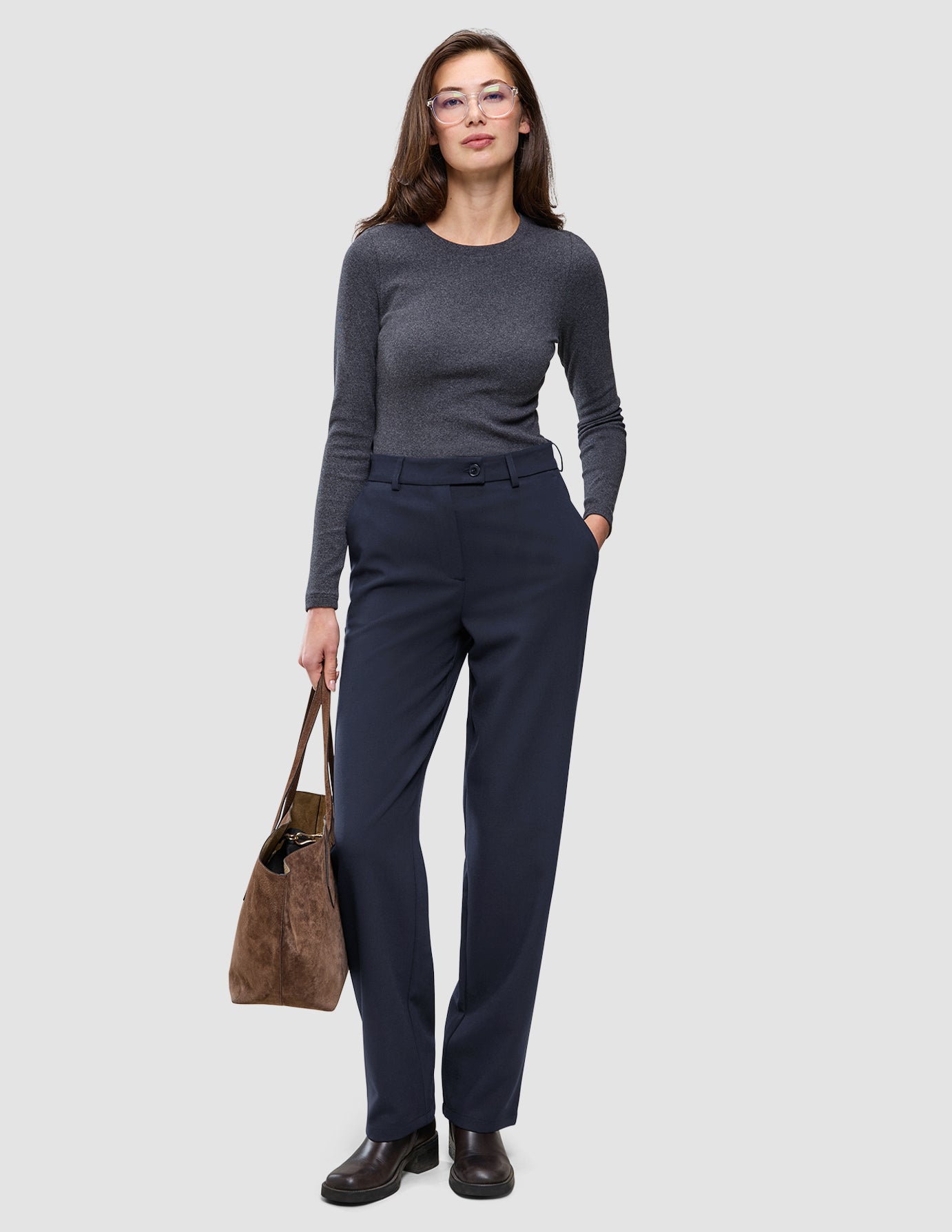 En kvinne i en grå topp med lange ermer og Women GO2-bukser i modell Straight Blue Nights, som holder en brun bæreveske.