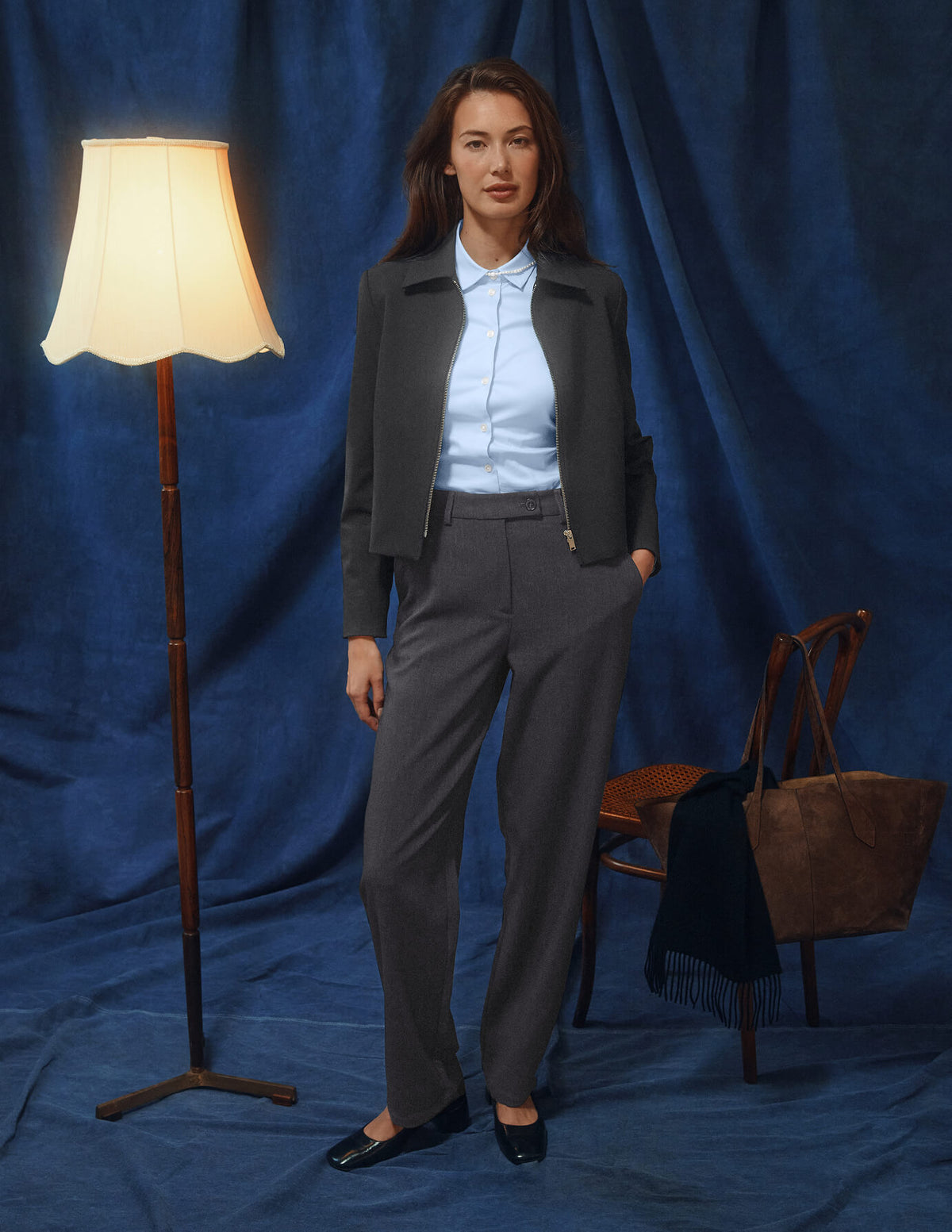 En kvinne har på seg en mørkegrå jakke, en lyseblå skjorte med knapper og Women GO2 Pants Straight Dark Grey Melange.
