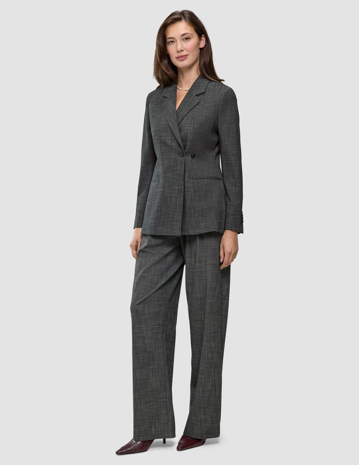 En kvinne har på seg en Women Nara Blazer Fitted Black Check i mørkegrå rutemønster, sammen med matchende bukser med vid benåpning og 360°-stretch.