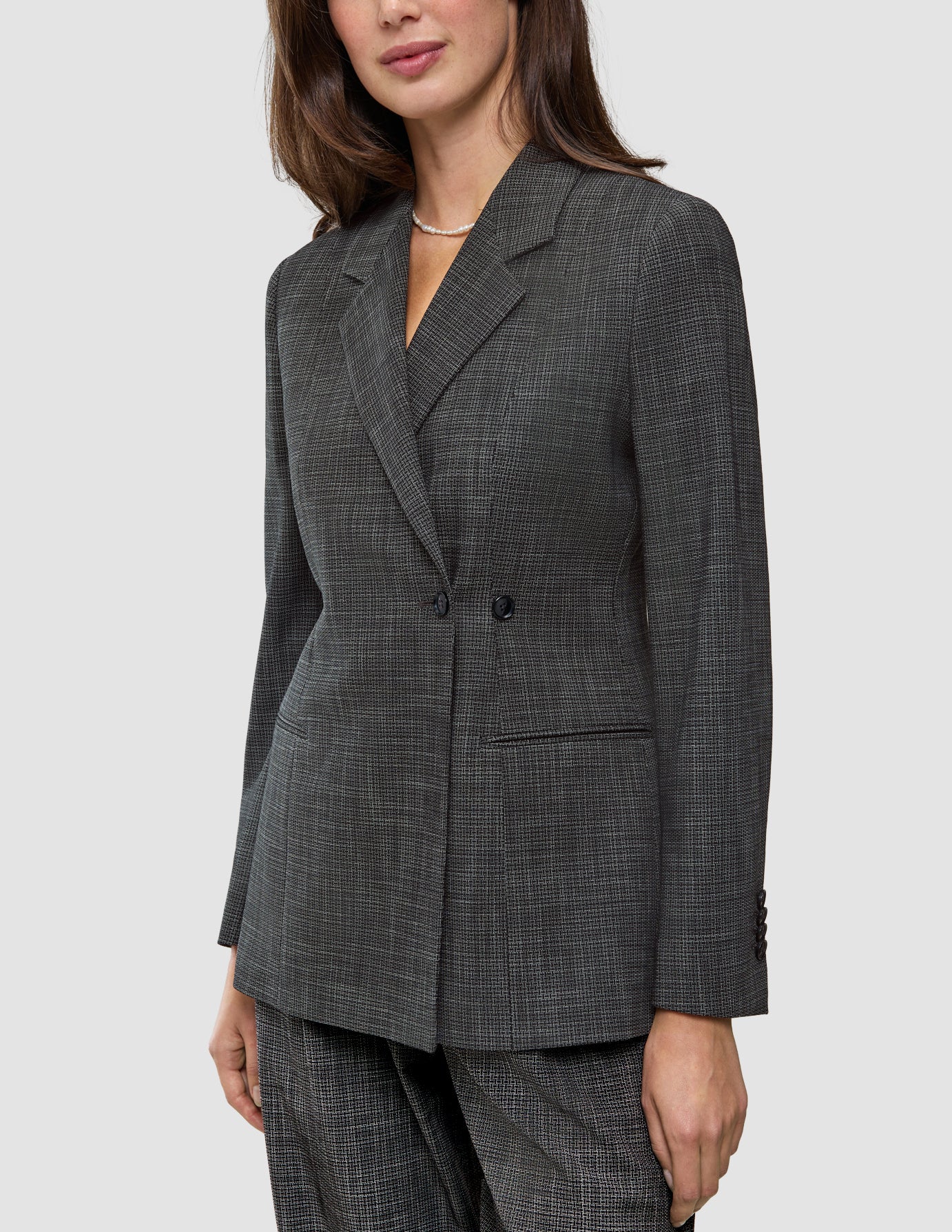 En kvinne iført en Women Nara Blazer Fitted Black Check – en skreddersydd blazer i kullgrått med dobbeltspent knappestolpe og rutemønster.