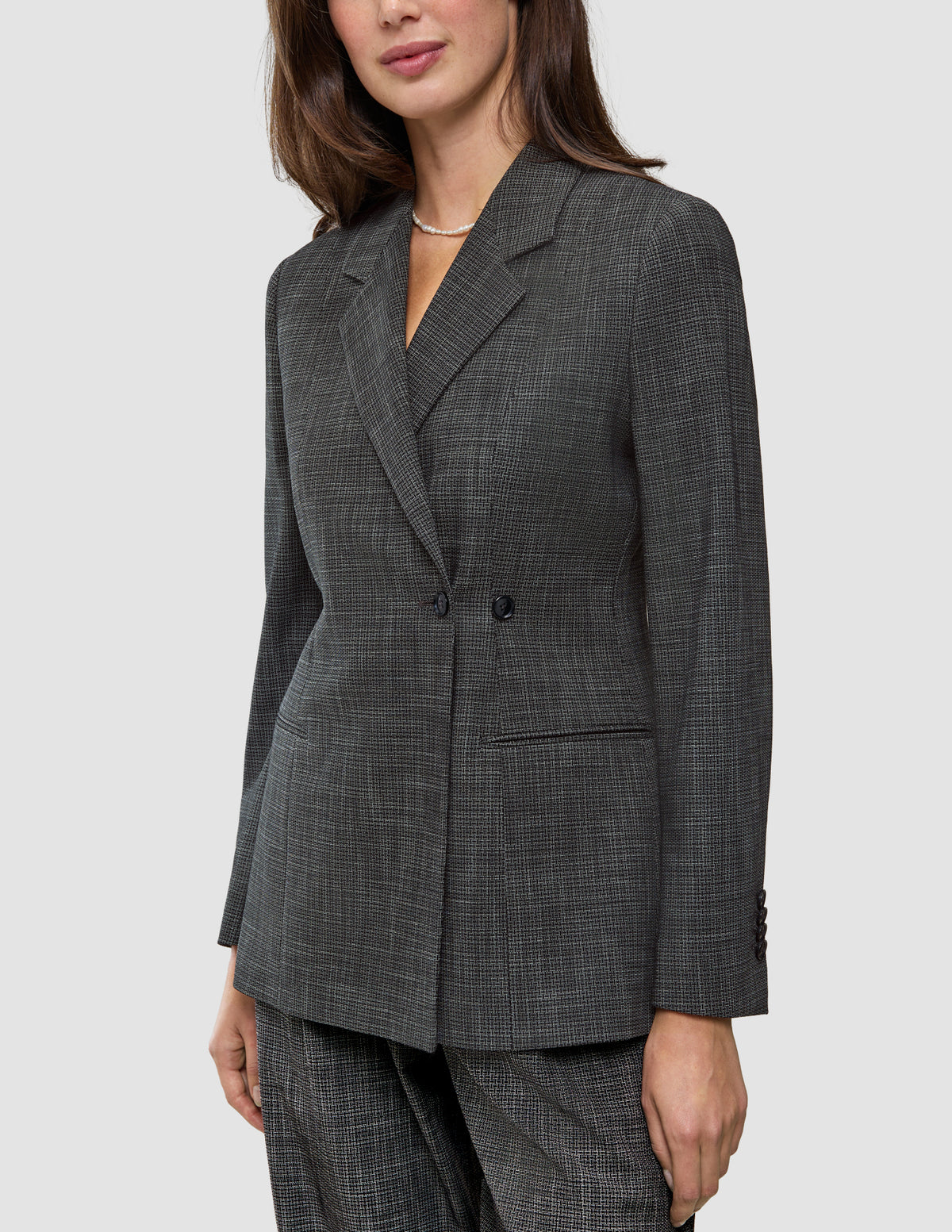 En kvinne iført en Women Nara Blazer Fitted Black Check – en skreddersydd blazer i kullgrått med dobbeltspent knappestolpe og rutemønster.