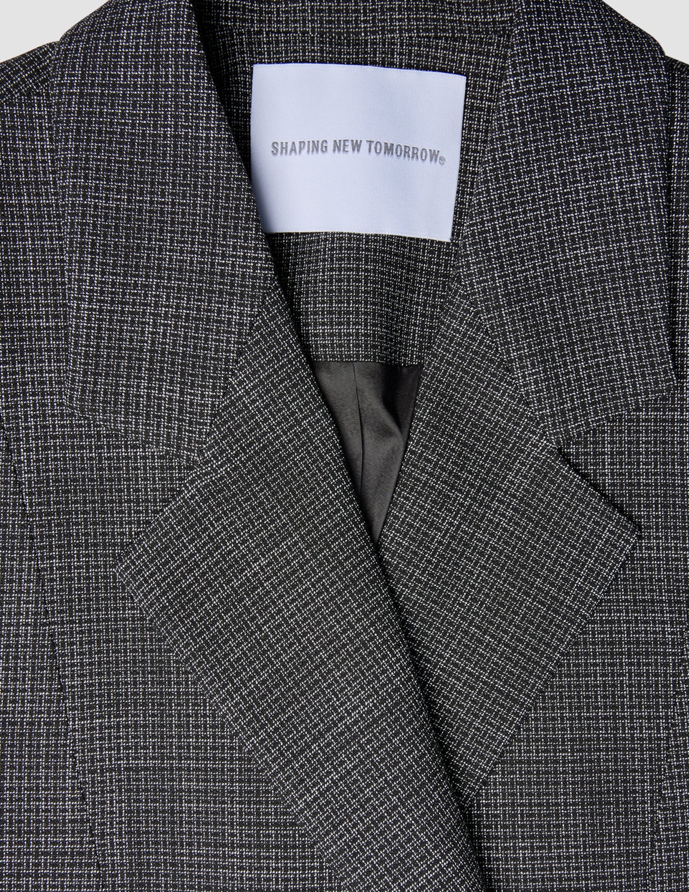 Nærbilde av en svart- og hvitrutet Women Nara Blazer Fitted Black Check med et SHAPING NEW TOMORROW-merke i nakken.