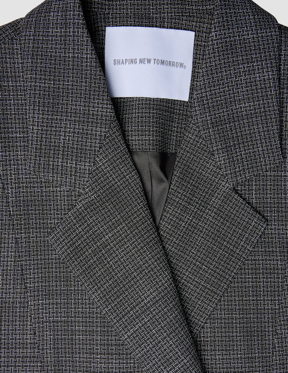 Nærbilde av en svart- og hvitrutet Women Nara Blazer Fitted Black Check med et SHAPING NEW TOMORROW-merke i nakken.