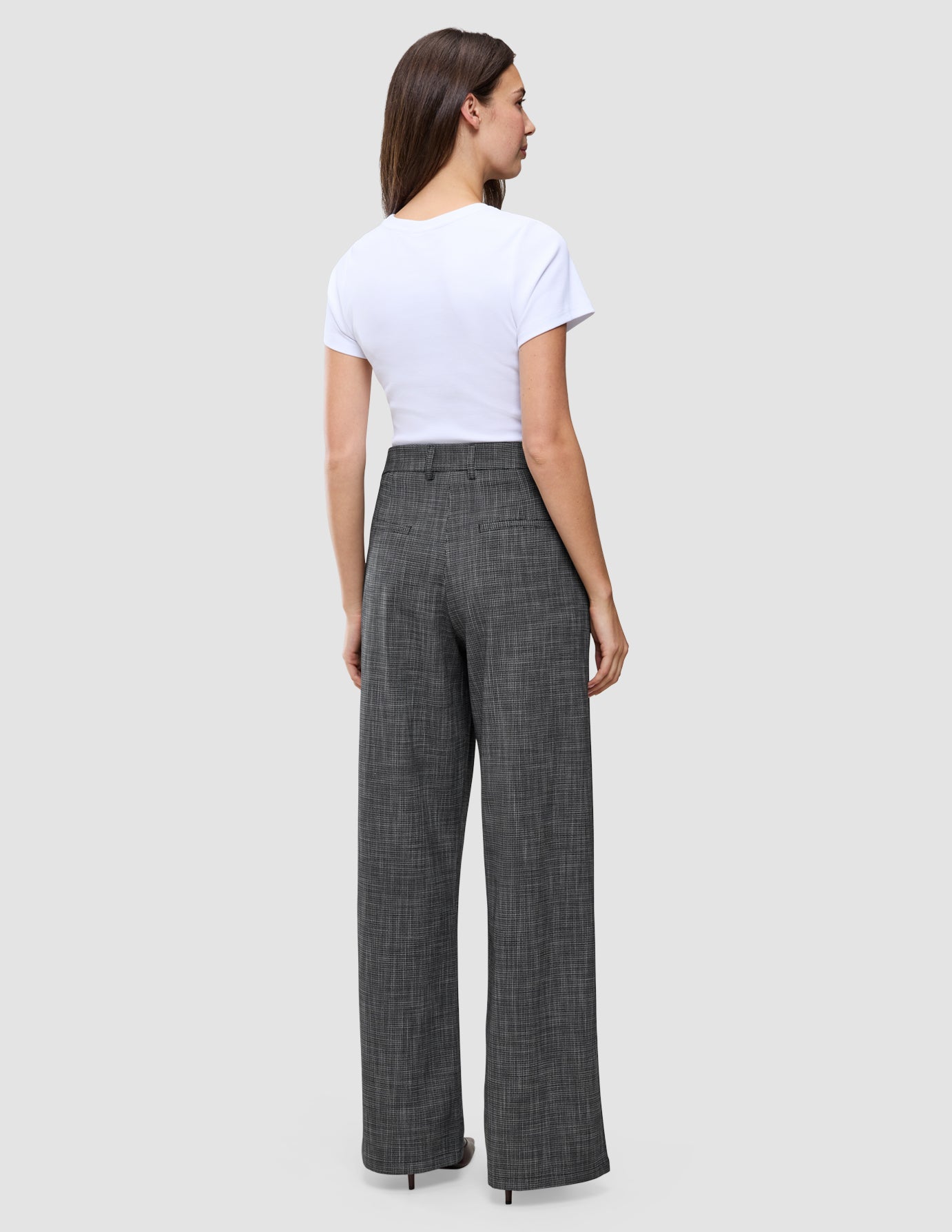 En person sett bakfra, kledd i en hvit T-skjorte og Women Nara Pants Wide Black Check med et diskret rutemønster.