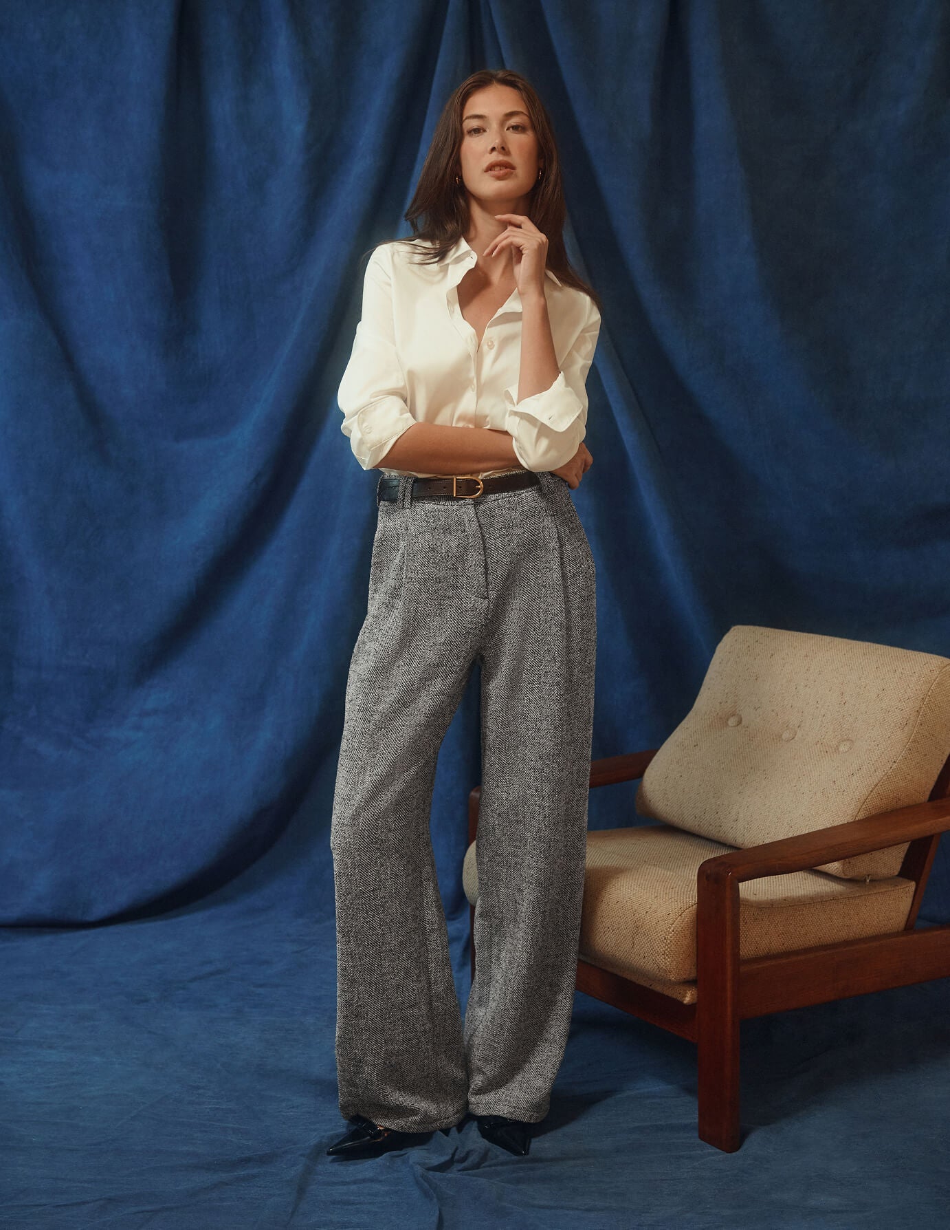 En kvinne har på seg en Women’s Oxford Shirt White Orchid Slim, som er stappet inn i grå bukser med vid benvidde i et minimalistisk design.