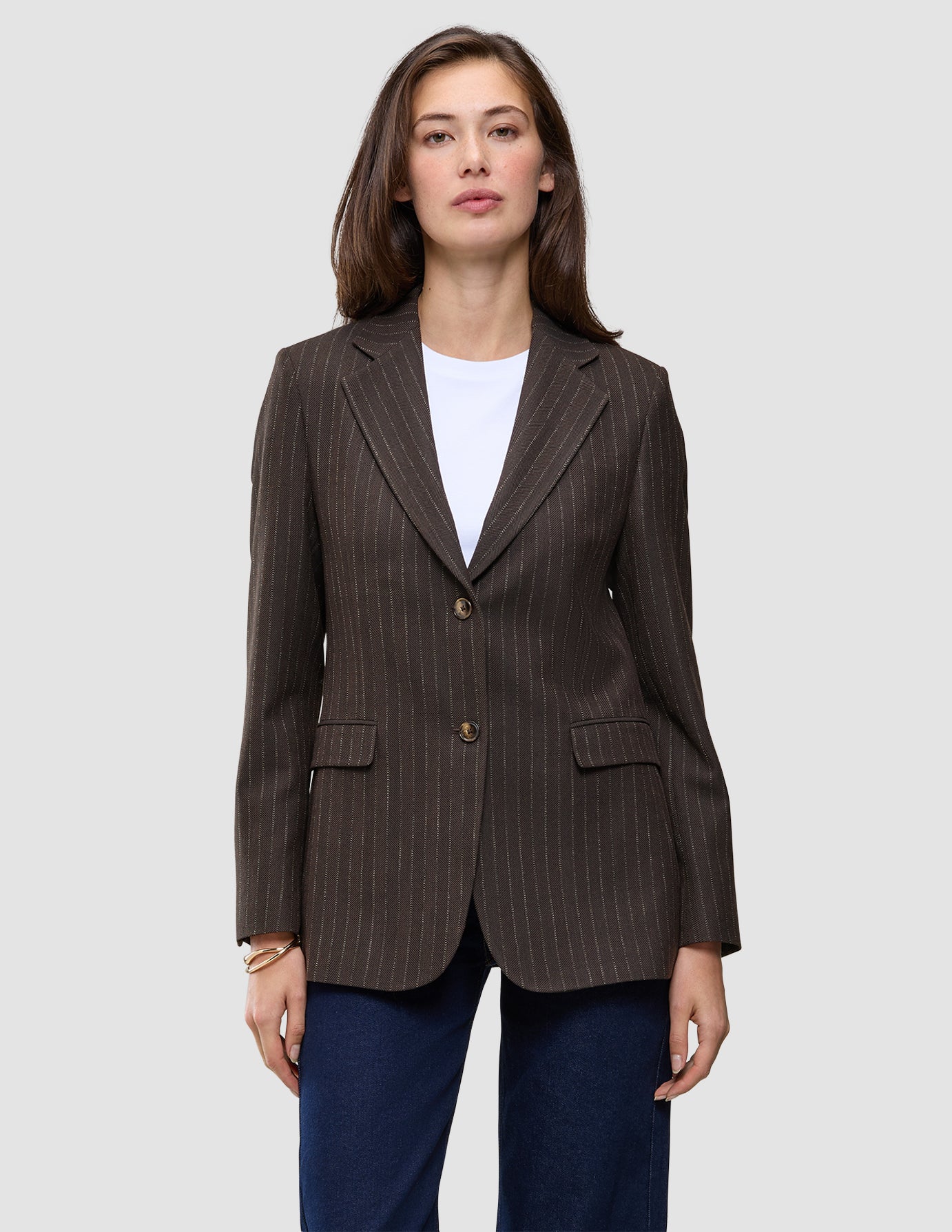 En kvinne har på seg en Women Serene Blazer Regular Walnut Herringbone over en hvit T-skjorte og blå jeans.