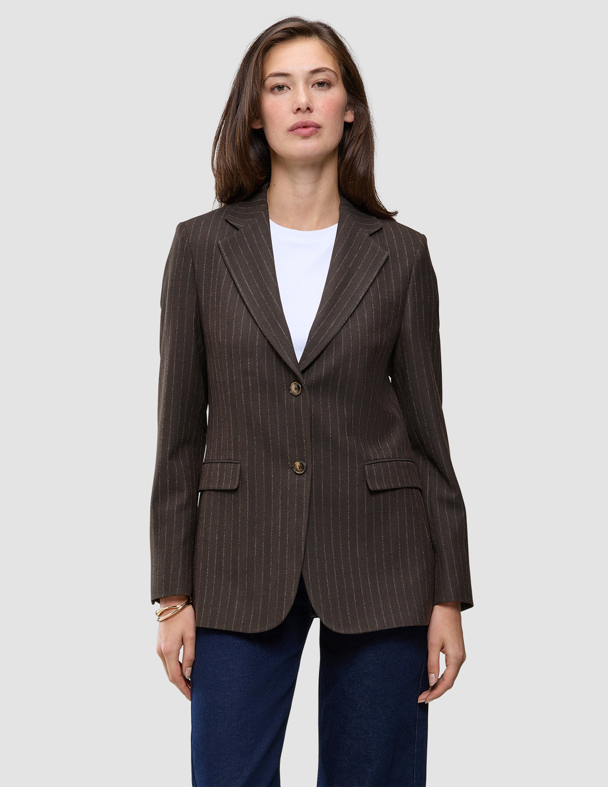 En kvinne har på seg en Women Serene Blazer Regular Walnut Herringbone over en hvit T-skjorte og blå jeans.