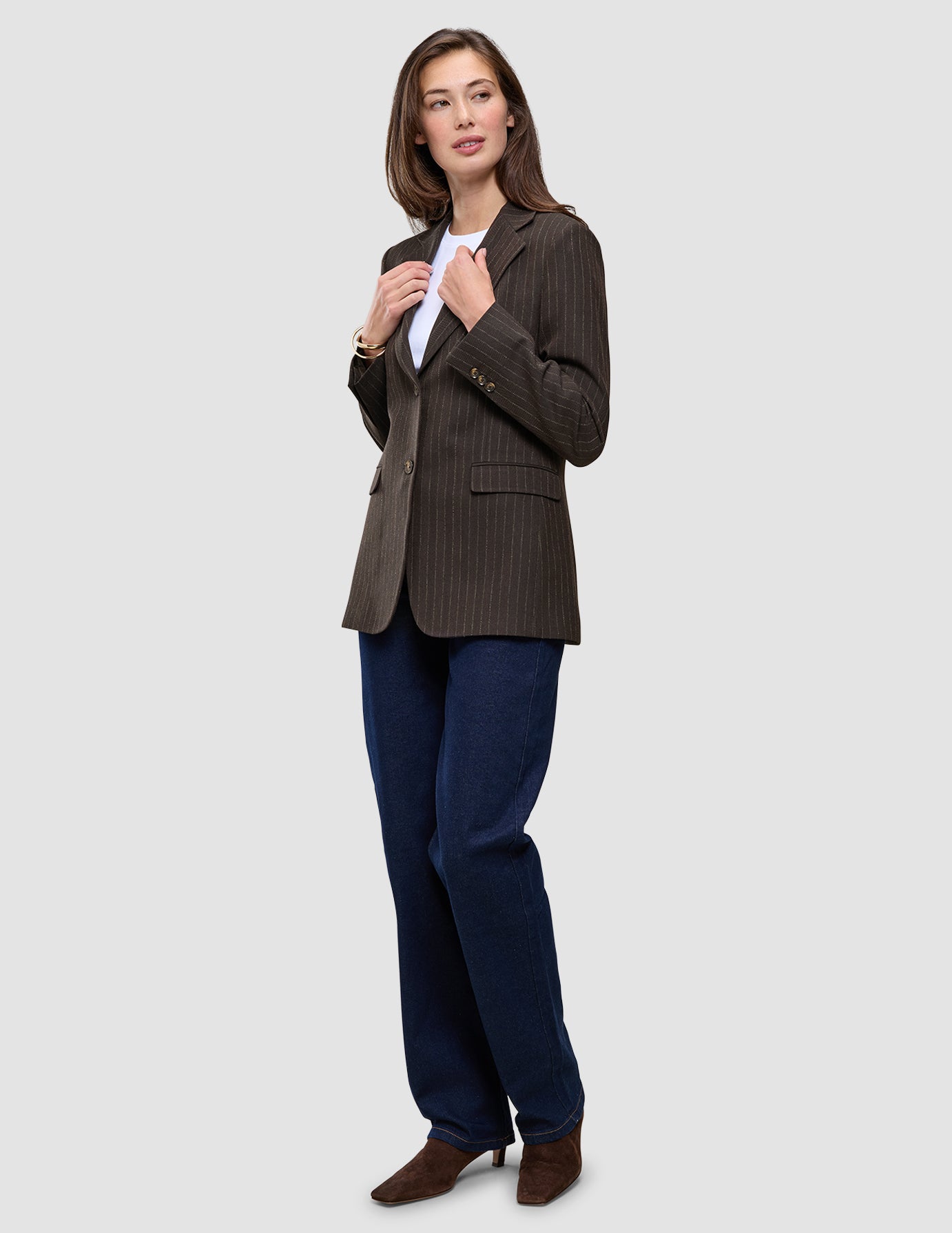 En kvinne har på seg en Women Serene Blazer Regular i valnøttfarget fiskebeinmønster over en hvit skjorte og blå jeans, noe som gjenspeiler en klassisk stil.