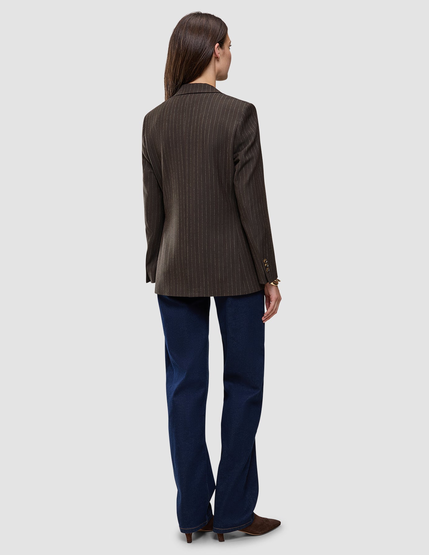 Sett bakfra har personen på seg en Women Serene Blazer Regular Walnut Herringbone, mørkeblå jeans og brune sko.