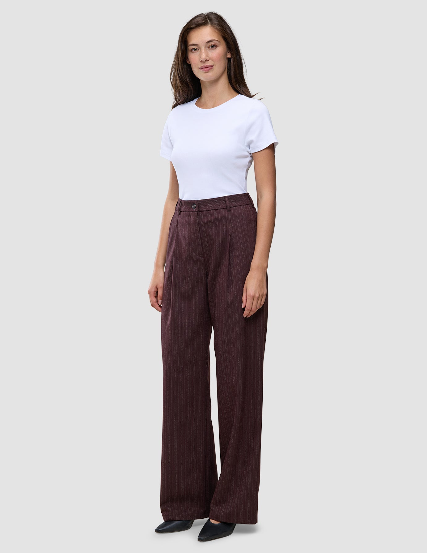 Kvinne iført en hvit T-skjorte og et par rødbrune Women Serene Pants Wide Berry Pinstripe-bukser med vid benvidde og tynne striper.