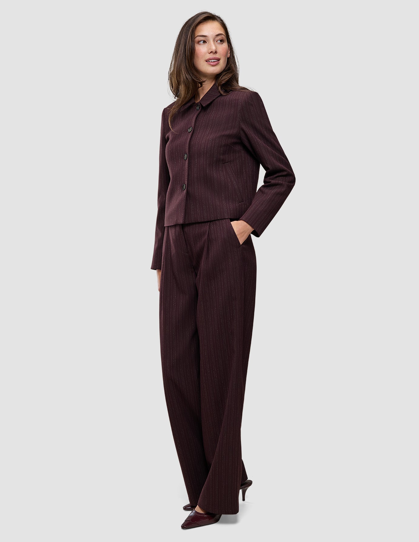 En kvinne kledd i en minimalistisk Women Serene Short Jacket Berry Pinstripe og matchende bukser med vide ben.