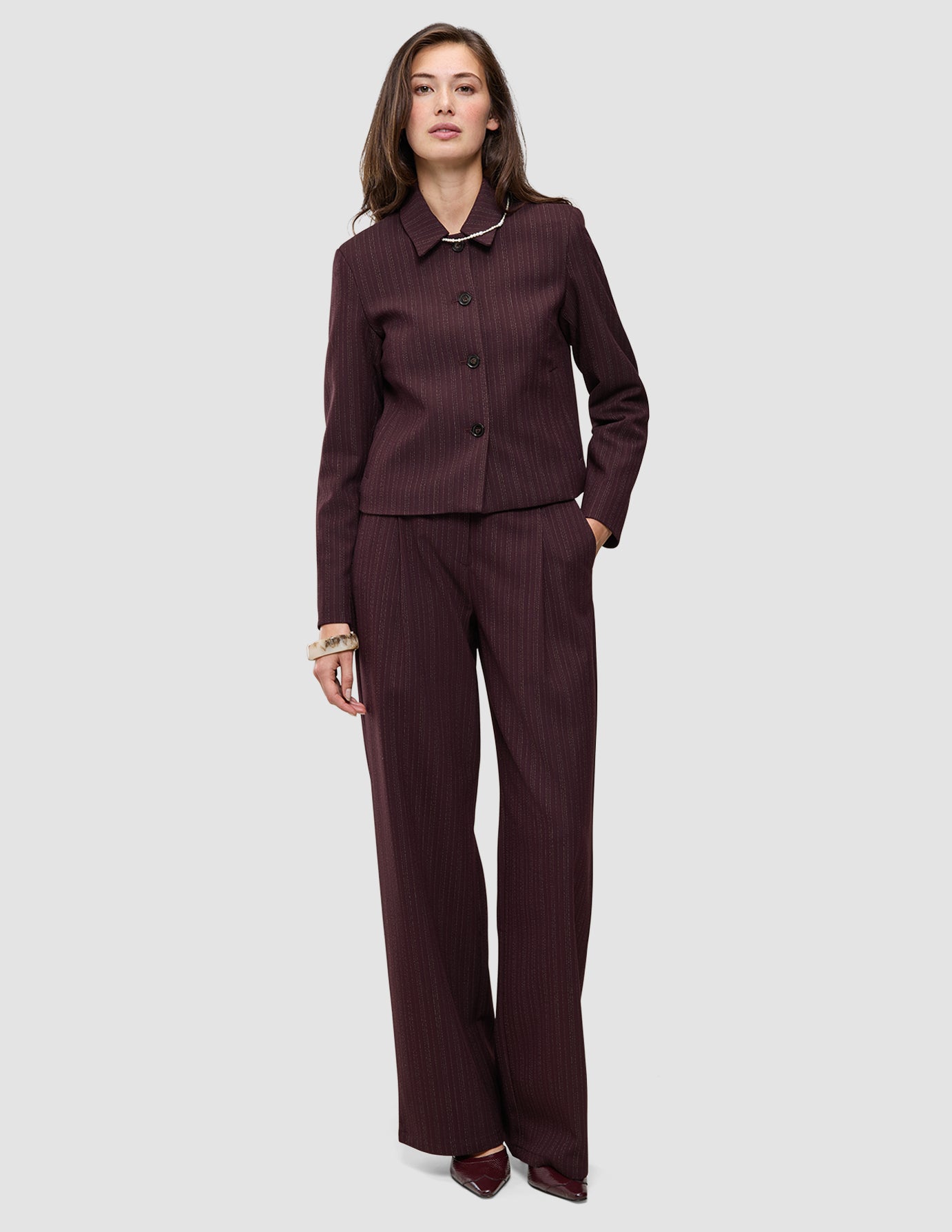 En kvinne iført en Women Serene Short Jacket Berry Pinstripe sammen med matchende bukser med vide ben.